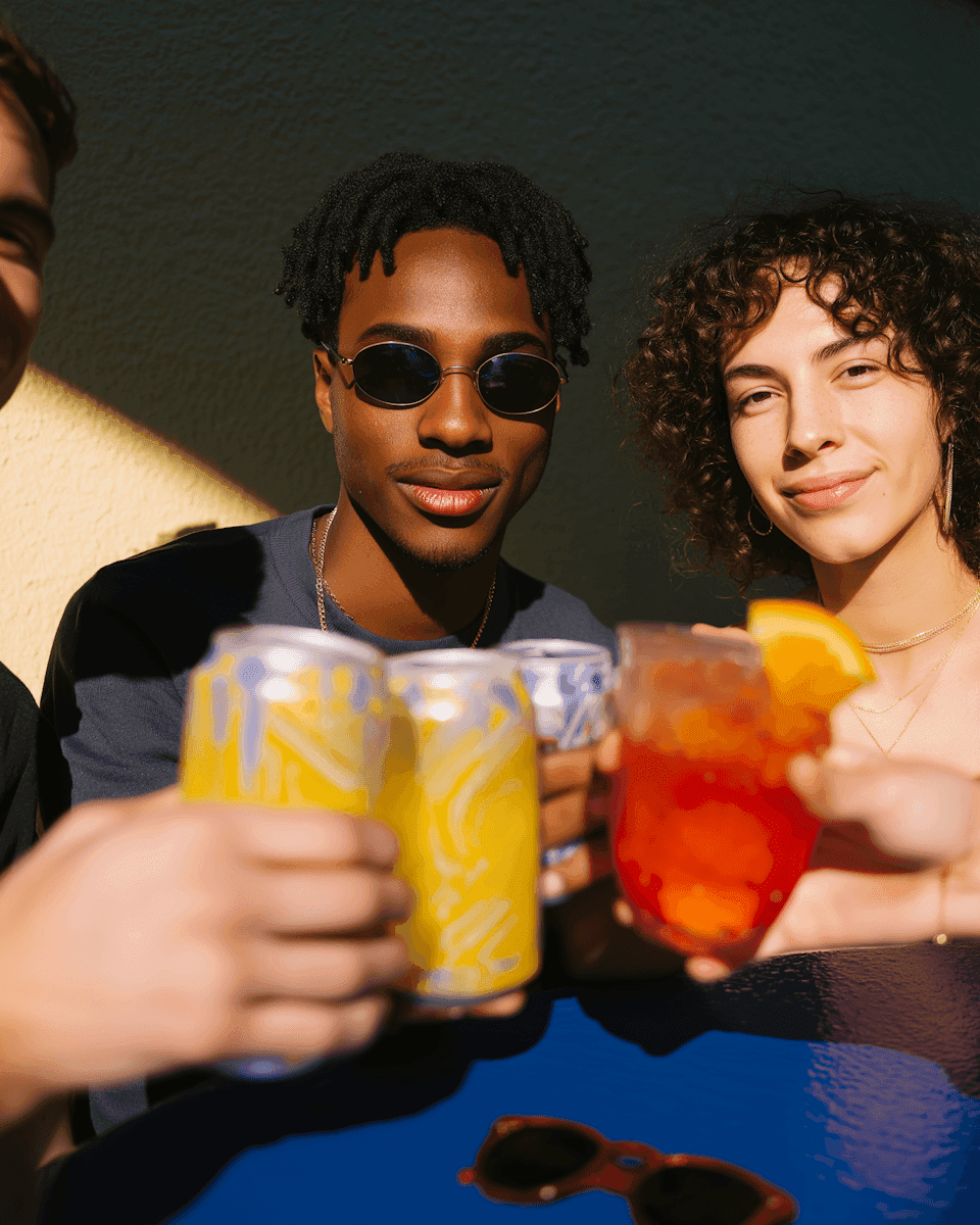 Friends raising cans and a cocktail in late afternoon sun